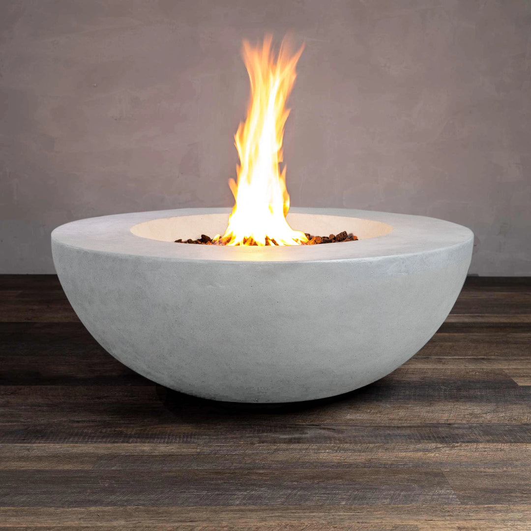 The Beton 42" White Round Concrete Fire Pit is displayed with the flame fully lit, offering a front view. The smooth concrete finish in white pairs elegantly with the intense flames rising from the central burner, surrounded by lava rocks. This natural gas fire pit includes a push-button ignition system for ease of use. It’s perfect for modern outdoor decor, providing both function and beauty to patios or backyard areas.