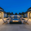 A symmetrical backyard fire pit area features a rectangular concrete fire pit positioned before a long swimming pool under a deep blue evening sky. Four wooden Adirondack chairs face the central fire feature, where steady flames burn cleanly, illustrating the benefits of a smokeless fire pit. The scene highlights the architectural balance and warm lighting of a modern residential courtyard at night.