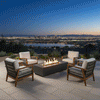 A luxury fire pit centers a stone-paved terrace overlooking a panoramic city skyline at twilight. Four cushioned chairs surround the fire table, creating an inviting space for conversation. The amber flames provide a stark contrast to the blue evening sky and distant city lights, showcasing the ambiance a propane fire pit adds to a family gathering fire pit setup on a high-altitude patio.