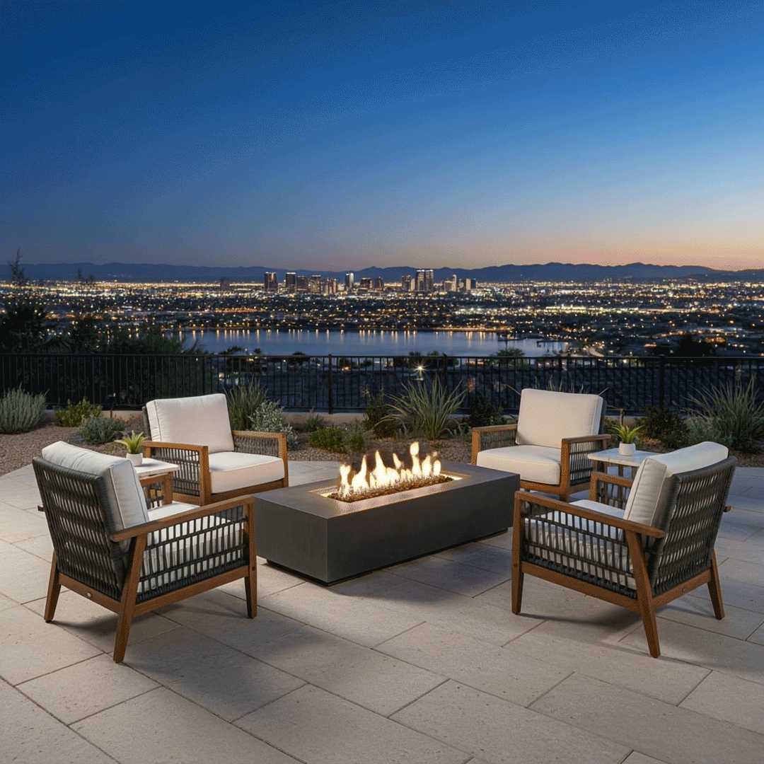 A luxury fire pit centers a stone-paved terrace overlooking a panoramic city skyline at twilight. Four cushioned chairs surround the fire table, creating an inviting space for conversation. The amber flames provide a stark contrast to the blue evening sky and distant city lights, showcasing the ambiance a propane fire pit adds to a family gathering fire pit setup on a high-altitude patio.