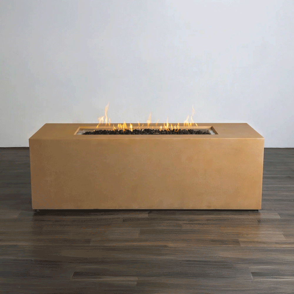 A studio view presents a rectangular concrete fire pit in a natural sand finish, resting on a dark wood floor against a white background. Bright orange flames rise continuously from a bed of black lava rocks along the length of the linear fire pit. The minimalist presentation emphasizes the smooth texture and steady flame height, demonstrating the clean operation of a natural gas fire pit connection.
