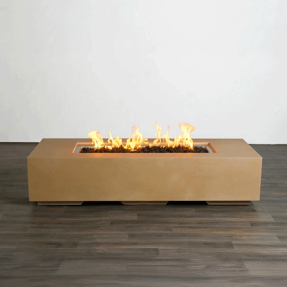 A studio view presents a rectangular concrete fire pit in a natural sand finish, contrasting against a dark wood floor and white background. Bright orange flames rise continuously from a bed of black lava rocks along the length of the linear fire pit, demonstrating the clean, smoke-free combustion. The minimalist presentation emphasizes the smooth texture and steady flame height typical of a high-quality natural gas fire pit connection.