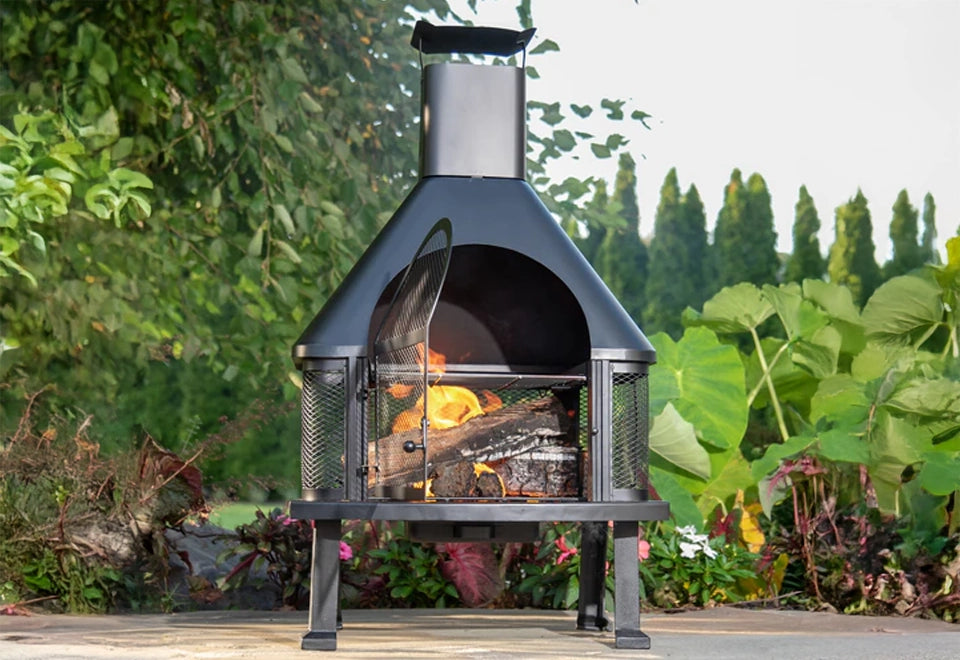 Traditional black metal chiminea with a tall chimney and mesh screen, showcasing a cozy wood-burning fire. The freestanding outdoor fire pit offers warmth and ambiance for backyard patios and garden settings, combining rustic charm with modern durability.