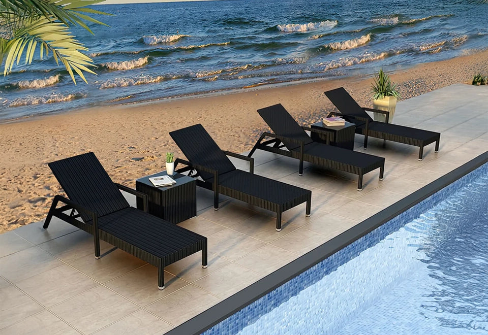 Set of black wicker chaise lounge chairs with adjustable backs, arranged poolside with a stunning view of the beach and ocean waves in the background.