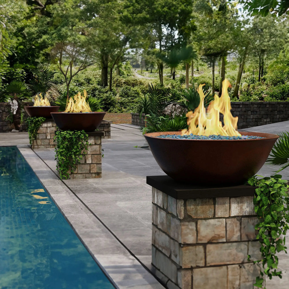 Campana Moreno 31-inch round copper fire bowls by Starfire Designs, elegantly placed poolside with blue fire glass and dynamic flames, creating a luxurious outdoor ambiance in a lush, natural setting