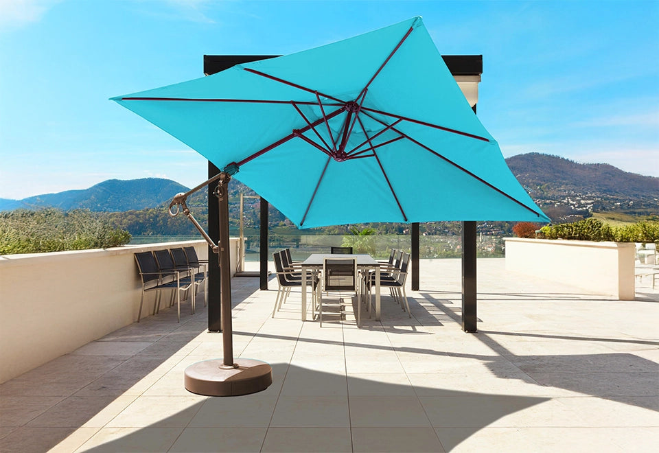 Modern cantilever patio umbrella with a vibrant blue canopy providing shade over a sleek outdoor dining area, offering a stunning view of rolling hills and a serene lake.