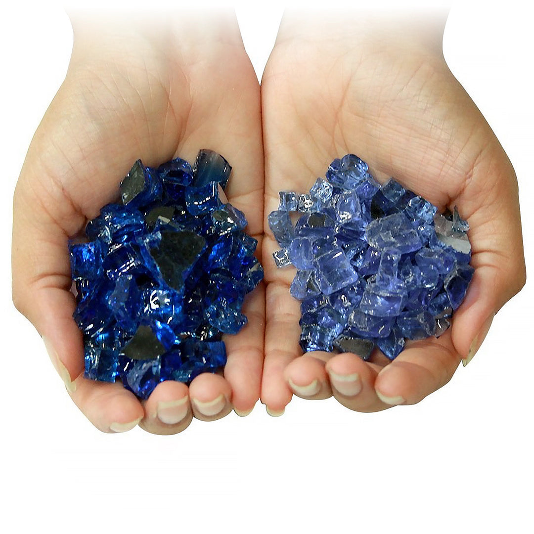 lose-up of hands holding two different types of blue fire pit glass, showcasing the difference in texture and color between dark blue reflective glass and lighter blue transparent glass