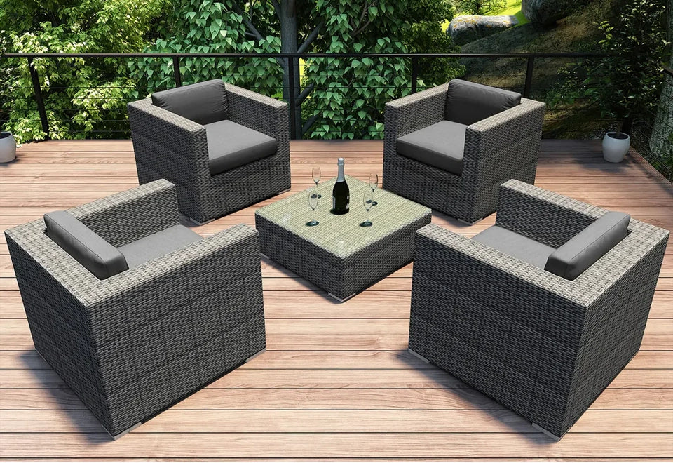 Modern outdoor patio set with four grey wicker club chairs and a matching coffee table on a wooden deck surrounded by greenery