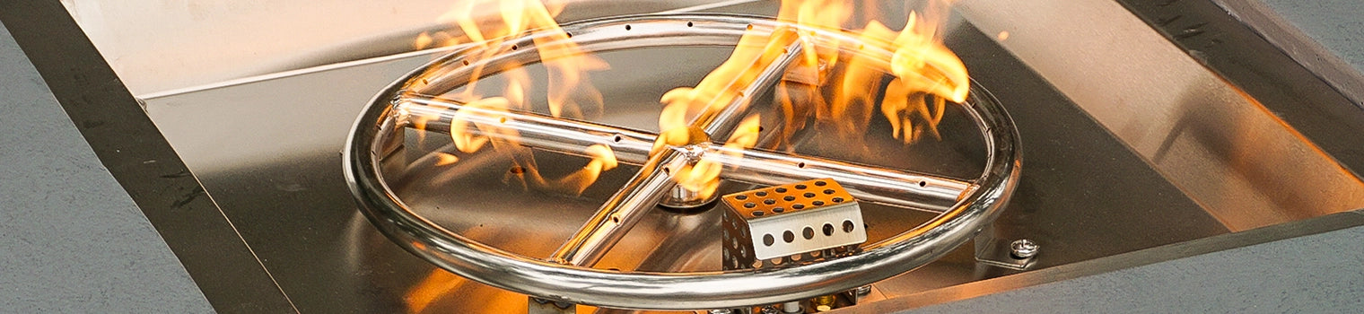 Stainless steel fire pit burner ring with active flames, installed in a square fire pit pan.