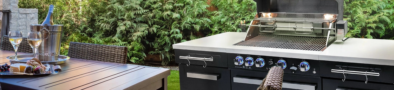 Modern outdoor kitchen island with built-in grill, accompanied by a dining table set with a wine bucket, glasses, and appetizers, in a lush garden setting