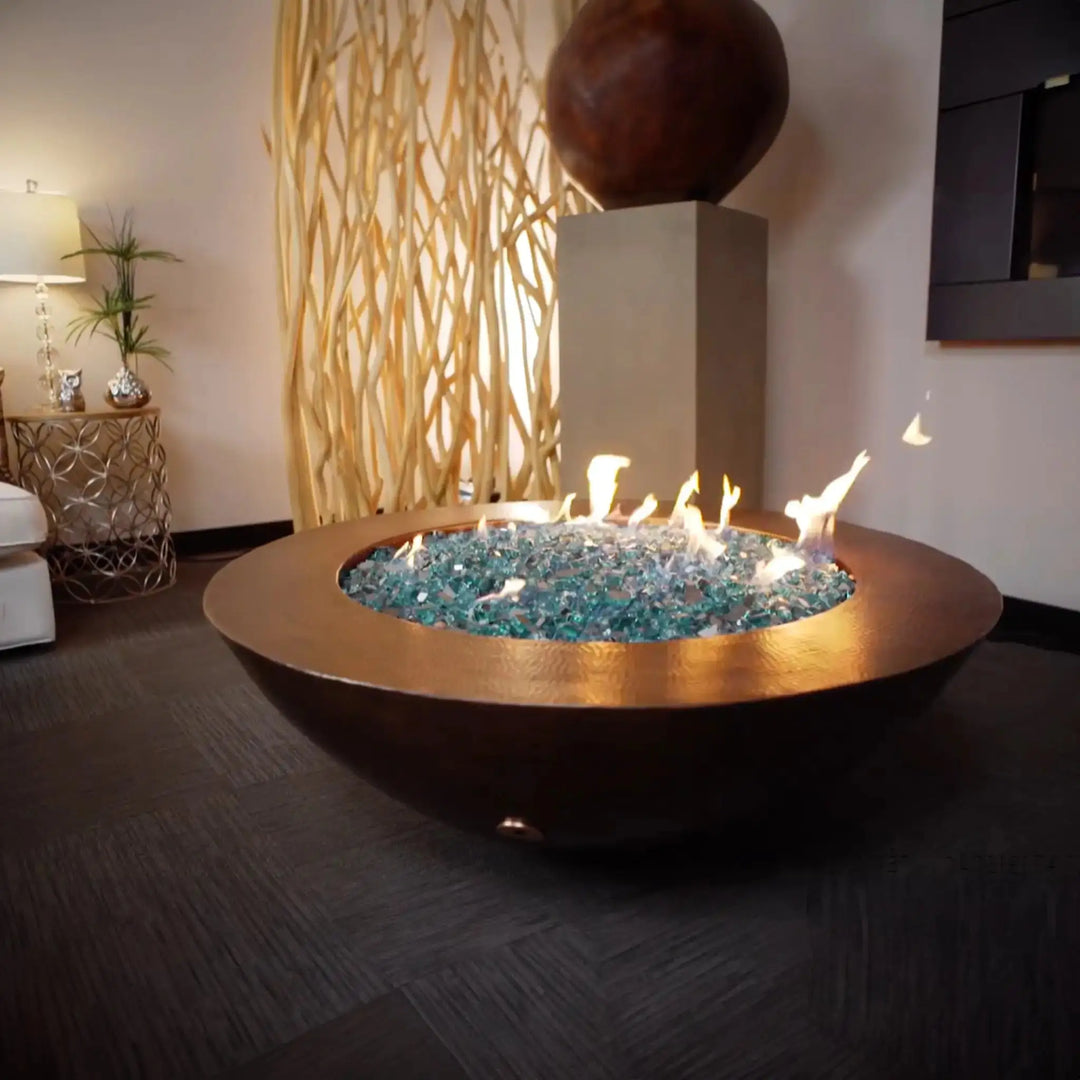 Cono Moreno 42-inch Round Copper Fire Pit elegantly displayed indoors, featuring a hand-hammered copper finish with vibrant blue fire glass, ideal for adding warmth and style to luxurious indoor spaces