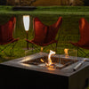 A luxurious EcoSmart Fire Base 40 fire pit set on a stylish outdoor patio with modern armchairs and warm-toned architecture. The sleek rectangular fire pit features a glass wind guard, creating a captivating ambiance. Perfect for an outdoor fire pit setup that enhances backyard gatherings with a natural gas fire pit or ethanol fire pit experience.

