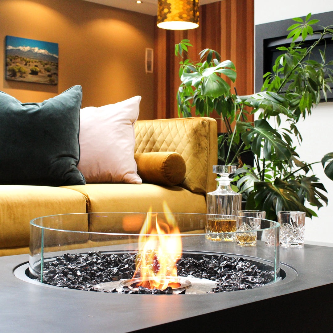 A close-up of the EcoSmart Fire Martini 50 outdoor fire bowl, elegantly styled in a chic indoor lounge with warm lighting. The flickering flames reflect on the black burner, adding to the cozy fire table atmosphere.