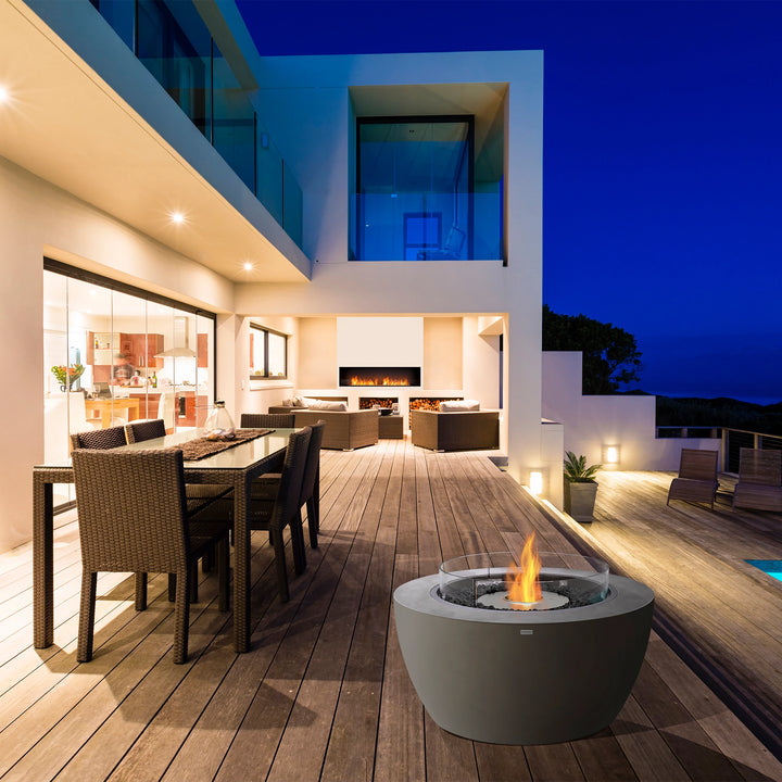 A luxurious outdoor gas fire pit setup featuring the EcoSmart Fire Pit Pod 40 on a high-end wooden deck with a panoramic nighttime view. The round gas fire pit with a glass wind guard and stainless steel burner emits a brilliant flame, adding warmth and sophistication to the outdoor dining and lounge area. Perfect for modern fire pit outdoor arrangements, this sleek design enhances the ambiance of a stylish outdoor entertainment space.