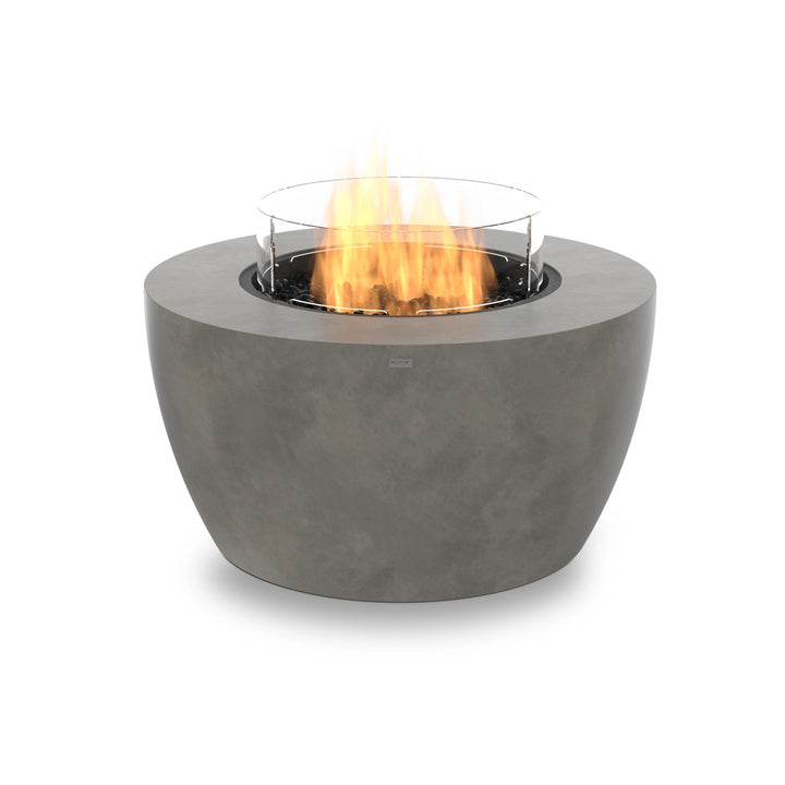 A round propane fire pit in natural concrete, featuring a glass wind guard, black fire media, and a contemporary fire table design. The EcoSmart Fire Pod 40 is a versatile fire bowl outdoor fire pit, ideal for stylish outdoor settings.