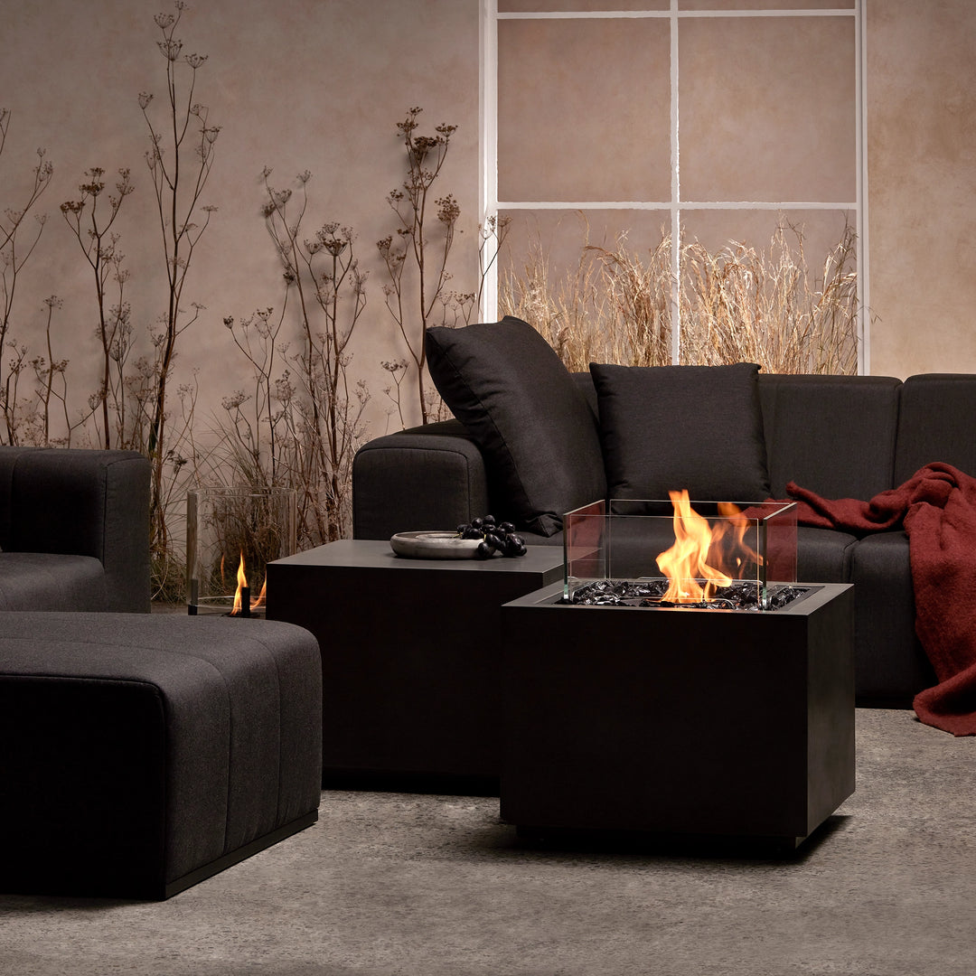 This image showcases the EcoSmart Fire Sidecar 24 in a modern indoor setting. The fire pit features a sleek black finish, glass wind guard, and black fire glass, providing a cozy atmosphere. Perfect for contemporary living spaces, the EcoSmart Fire Sidecar 24 is a stylish choice for creating warmth and ambiance in any modern lounge.