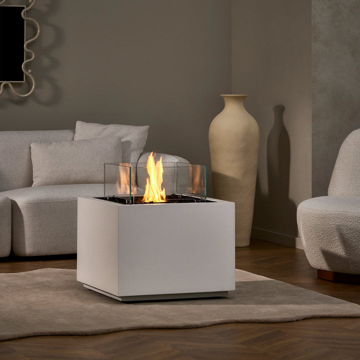 A lifestyle shot of the EcoSmart Fire Sidecar 24 placed in a bright white living room. The white finish complements the elegant and minimalistic décor, creating a soothing ambiance. The fire pit is surrounded by cozy furniture, with the flames offering a warm and inviting atmosphere. Ideal for any stylish living room or lounge area. 