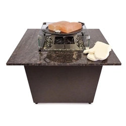 Square fire pit grill with a dark stone top, featuring a glass wind guard and integrated cooking surface. Includes grilling accessories like a heat-resistant glove, making it ideal for outdoor cooking and entertaining