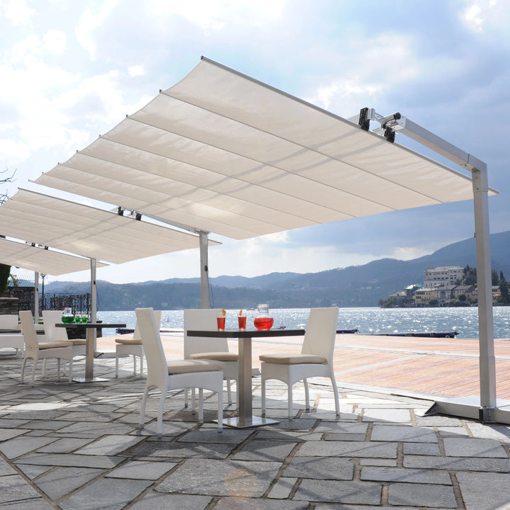 FIM Umbrellas Flexy 10' x 16' Rectangular Dual-Post Umbrella with a white canopy set in an elegant poolside outdoor setting. Featuring a robust dual-post design, this modern shade solution provides expansive coverage for seating areas, perfect for cafes, patios, and luxury settings. The sleek and minimalist structure blends seamlessly with the scenic waterfront, creating a sophisticated ambiance. Ideal for commercial or residential use, providing both style and sun protection