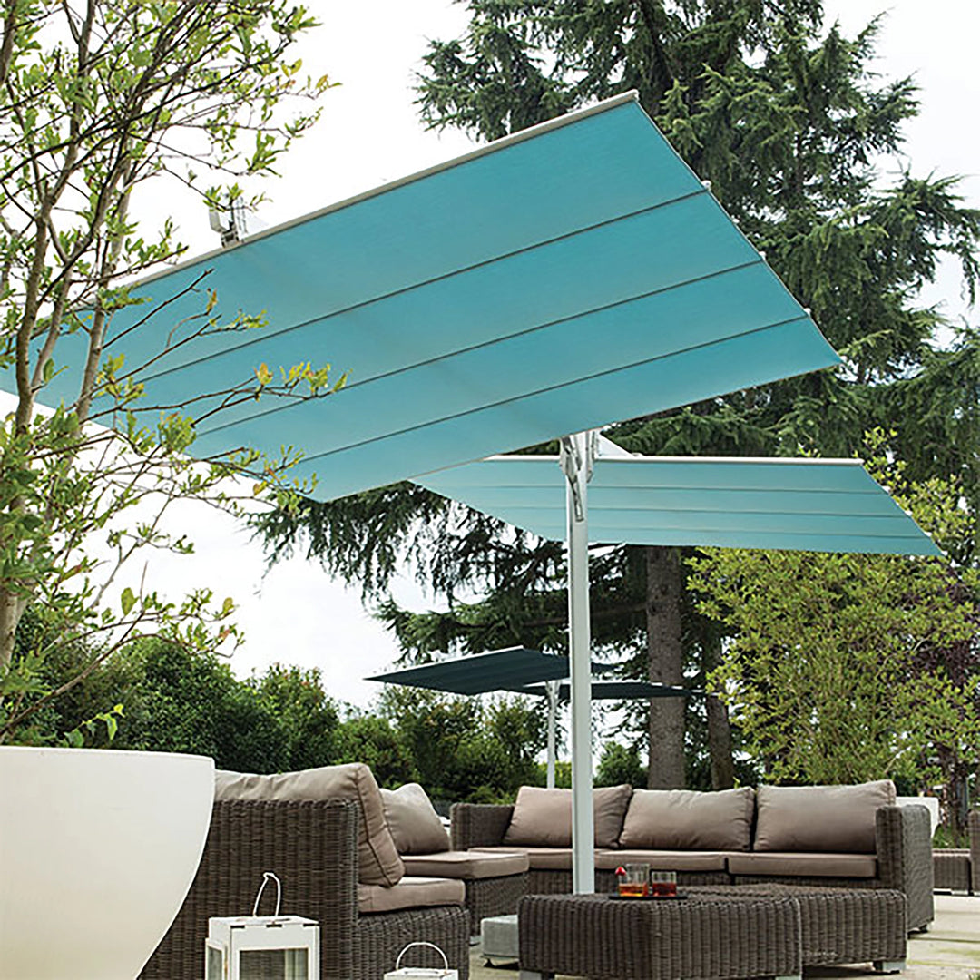 Front view of the FIM Umbrellas Flexy Twin 8x17' Rectangular Dual Shade Umbrella installed in a garden setting. The image displays the stylish dual shade canopy system blending perfectly with outdoor lounge furniture, providing extensive coverage for seating areas. The sleek and modern design adds a touch of elegance to any garden space.