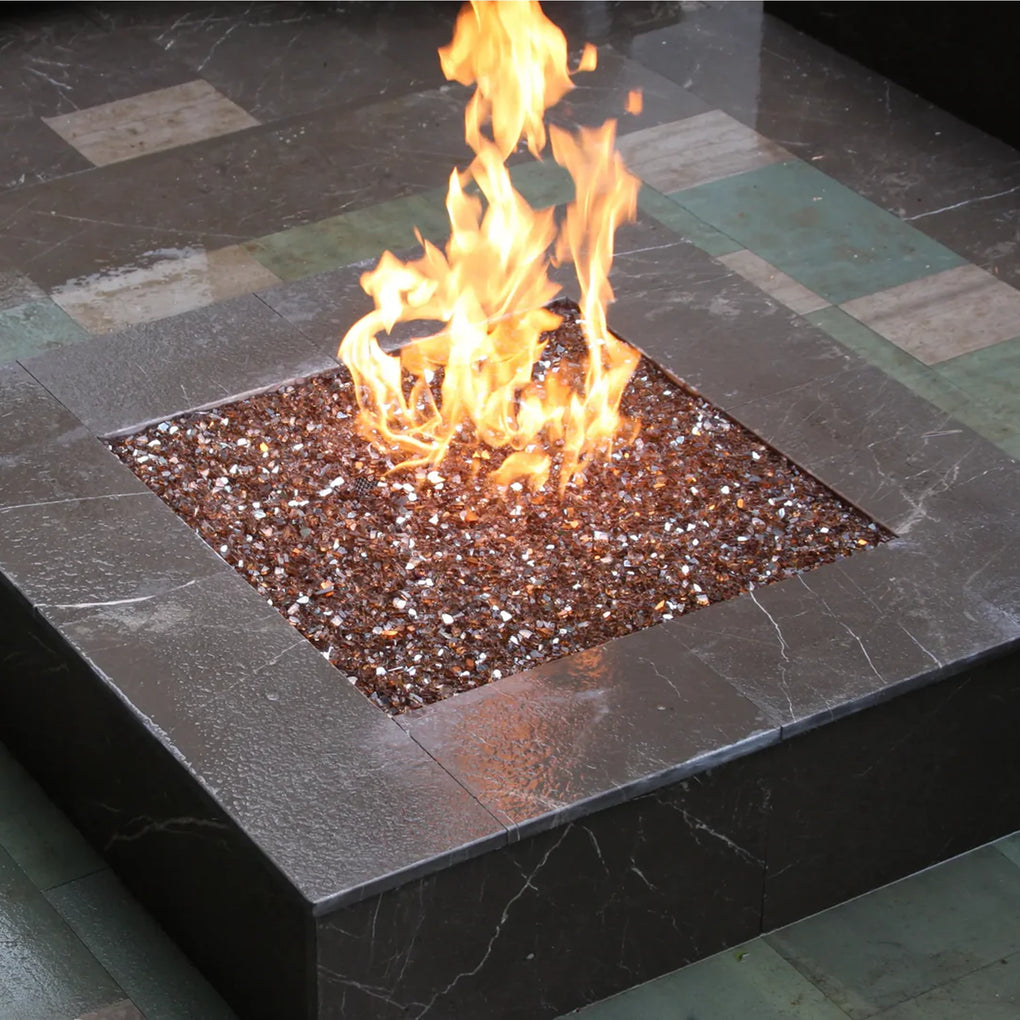 Modern square fire pit with brown reflective fire glass, creating a vibrant flame display on a tiled outdoor patio