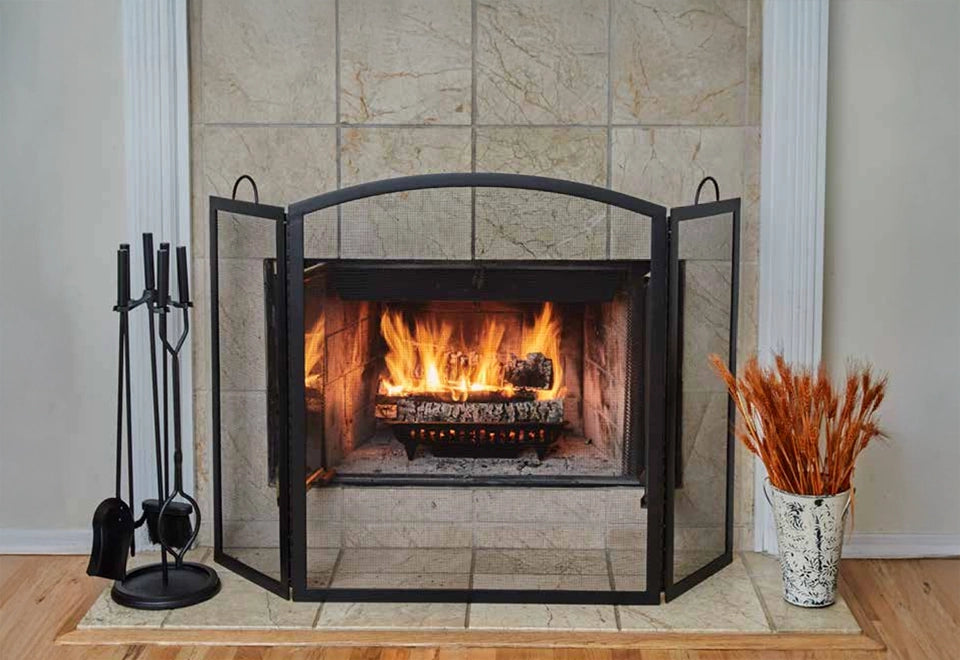 Black metal fireplace screen with open doors, featuring a set of fireplace tools and a crackling wood fire in a tiled hearth.