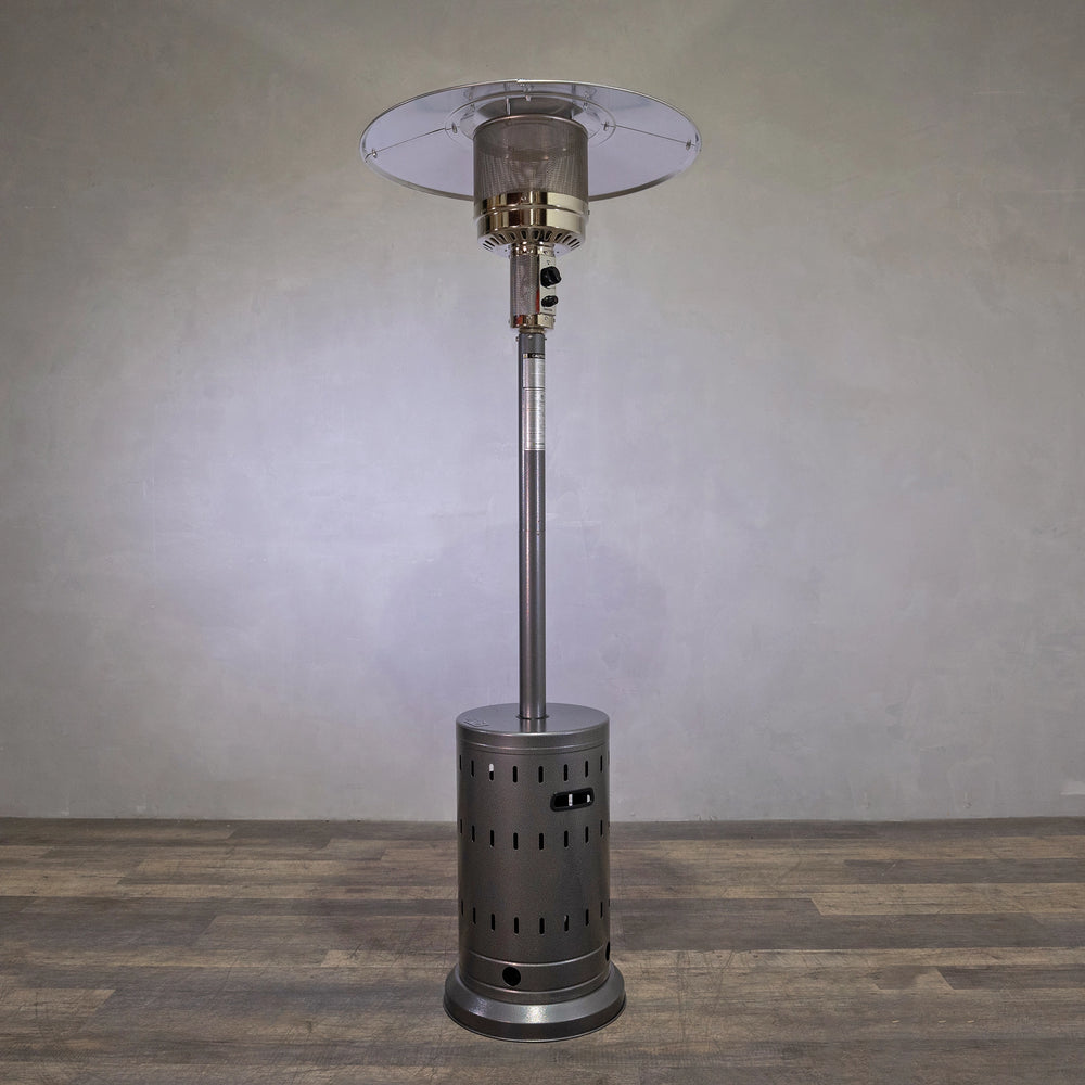 Golden Flame Outdoor Natural Gas Patio Heater in hammered silver finish, standing alone against a rustic wall. This patio heater offers efficient heat for outdoor spaces, with a sleek design that complements modern backyard or patio setups. Ideal for commercial and residential use. Perfect for natural gas outdoor heating, providing warmth during cool evenings.