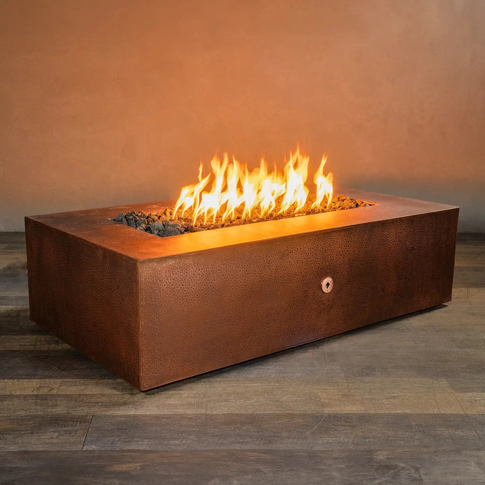 Angled view of the Gravity Moreno 60x32 rectangular copper fire pit by Starfire Designs, showcasing its hammered copper finish and wide burning area, ideal for creating a warm and inviting outdoor patio ambiance