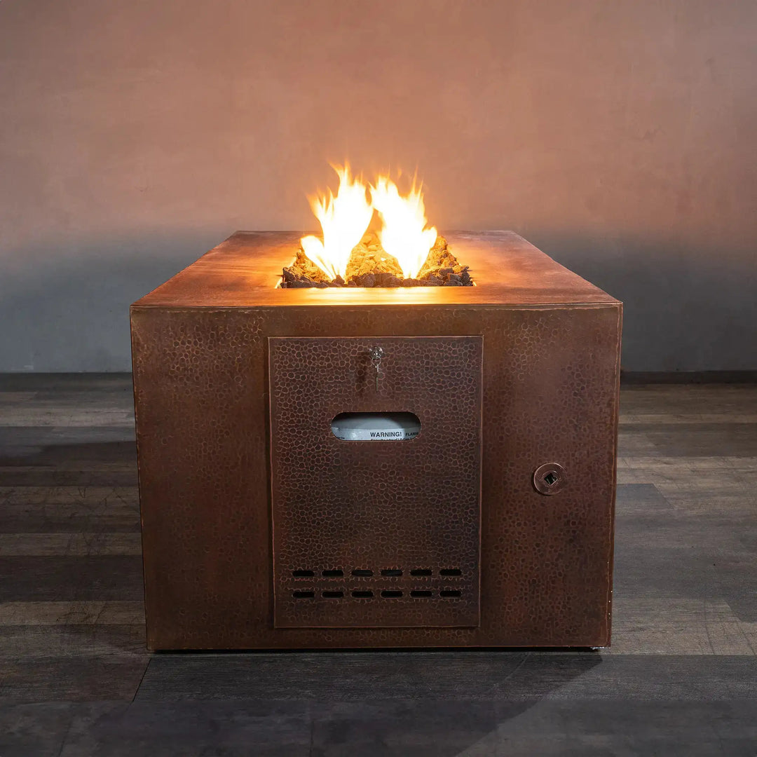 Front view of the Gravity Moreno 60x32 rectangular copper fire pit by Starfire Designs, showcasing the hidden propane tank compartment and the vibrant flames rising from the center, ideal for contemporary outdoor settings