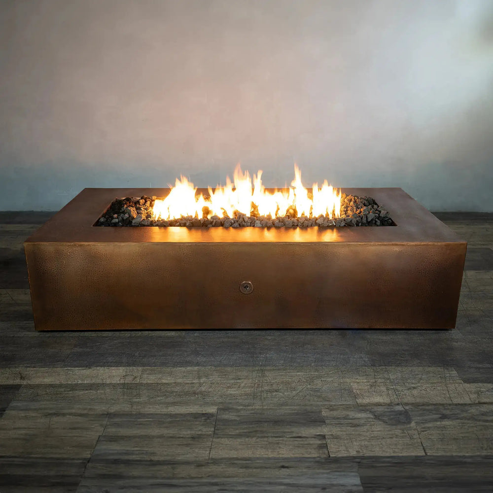 Gravity Moreno 72x38 copper fire pit by Starfire Designs, displaying a wide rectangular design with an active flame surrounded by black lava rocks, ideal for upscale outdoor settings