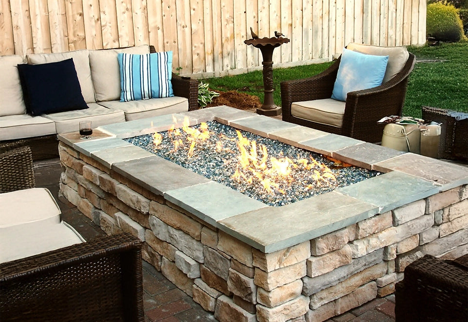 Outdoor stone fire pit with sparkling broken fire glass, surrounded by cozy patio seating and natural stone accents for a warm backyard ambiance.