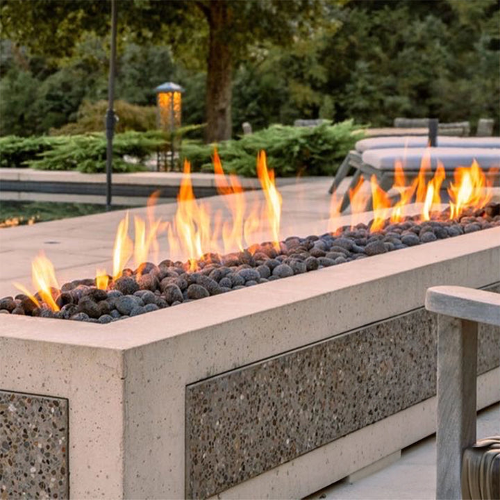 Outdoor rectangular concrete fire pit with burning flames and lava rocks, set in a modern patio with a natural background