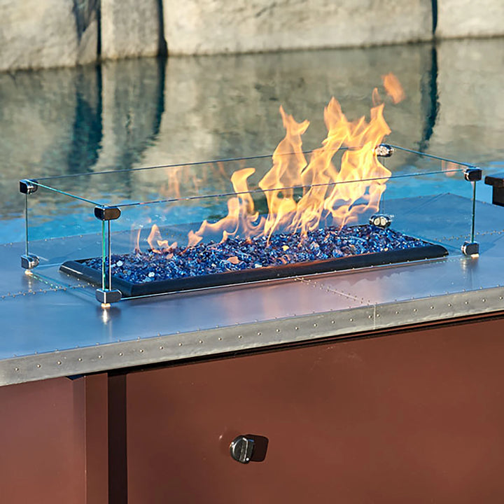 Close-up of the Linear Glass Flame Guard by American Fireglass, showcasing the tempered glass panels and chrome corner fittings. Designed for fire pits and fire tables, this wind guard enhances safety by protecting the flames from wind while maintaining a clear and unobstructed view. Perfect for use in various outdoor settings, offering a sophisticated and functional design for fire feature enthusiasts. This fire pit accessory is ideal for ensuring a consistent flame outdoors