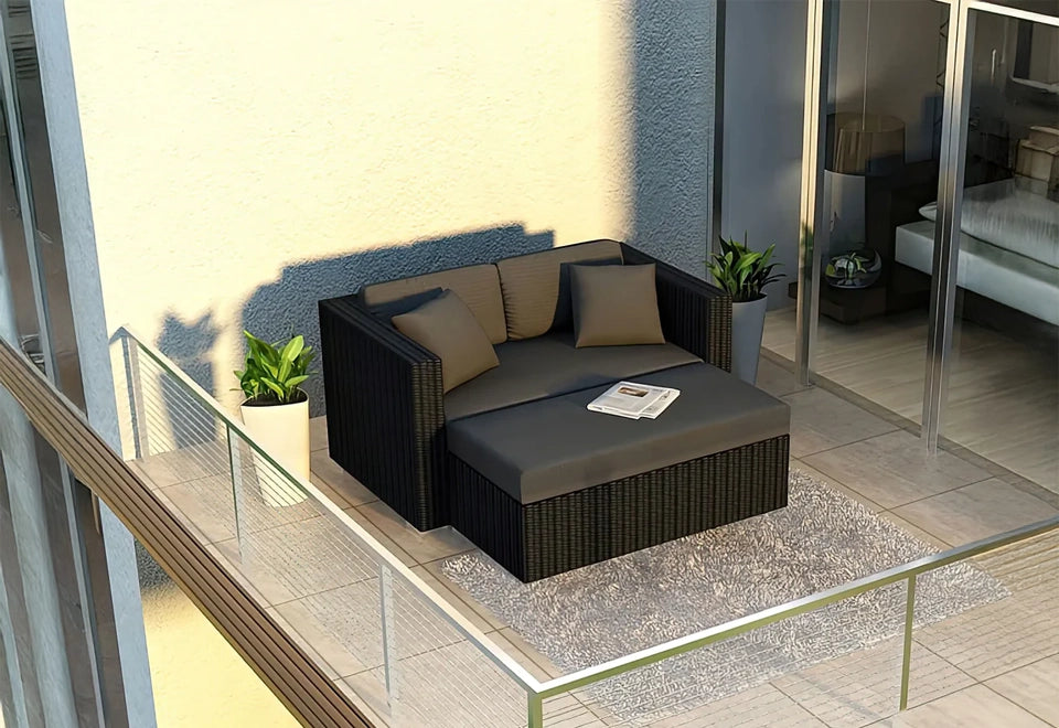 Modern black wicker loveseat with grey cushions on a sunny balcony, featuring a cozy rug and potted plants against a glass sliding door backdrop