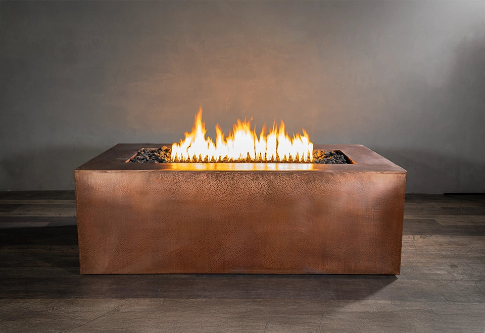 Luxury hammered copper rectangular gas fire pit with bright flames and lava rocks, adding warmth to a modern outdoor space.