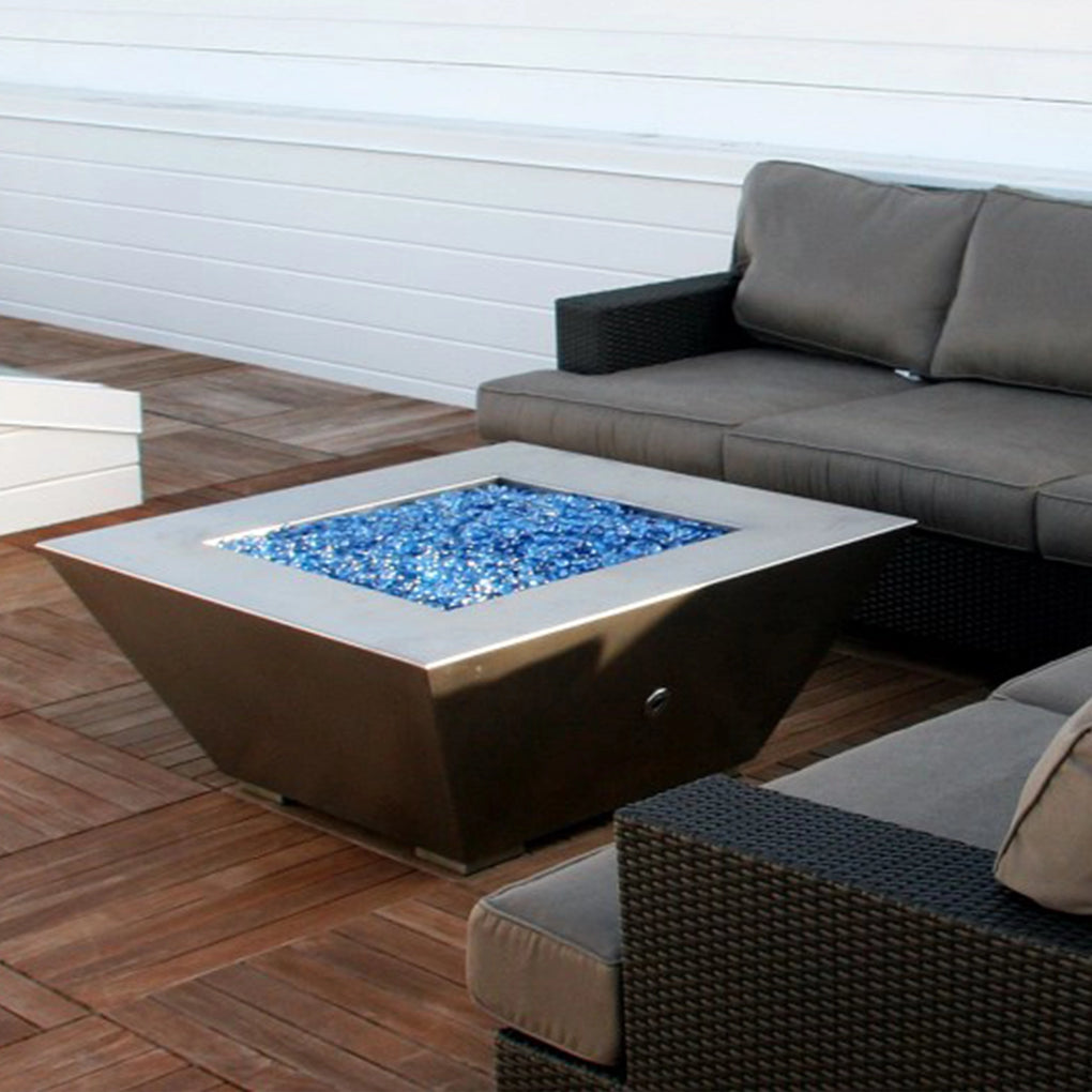 Modern patio with a square fire pit filled with blue fire glass, accompanied by cushioned outdoor seating on a wooden deck