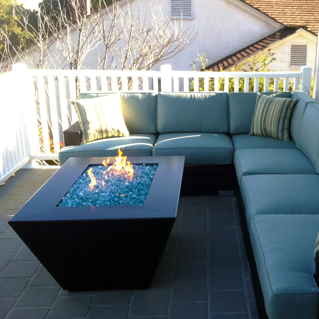 Outdoor patio with a modern sectional sofa and square fire pit filled with blue fire glass, creating a cozy and inviting seating area