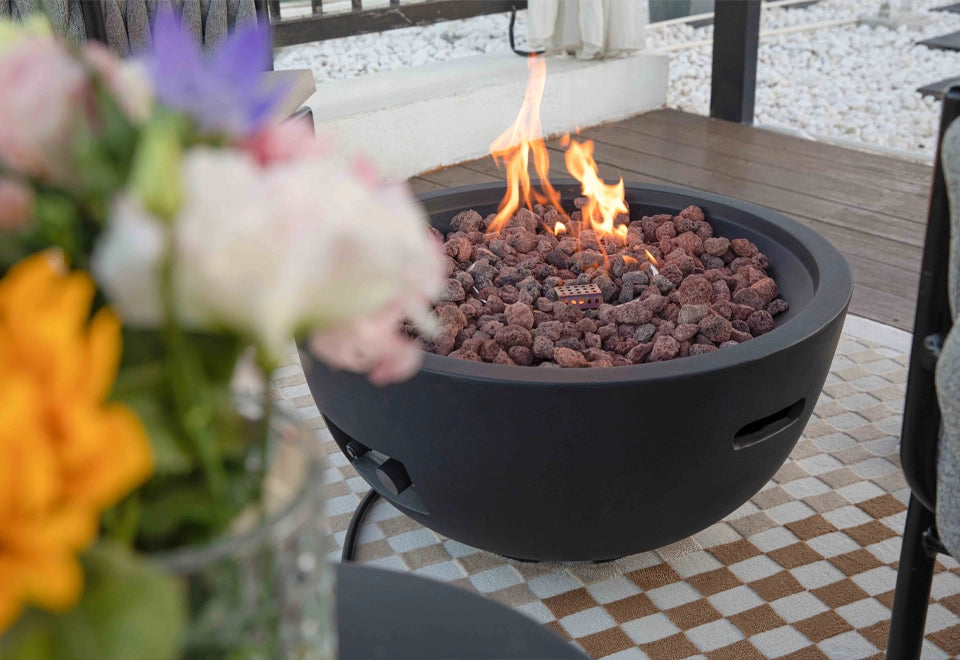 Modern black round fire pit with glowing lava rocks, creating a cozy ambiance on a stylish outdoor patio.