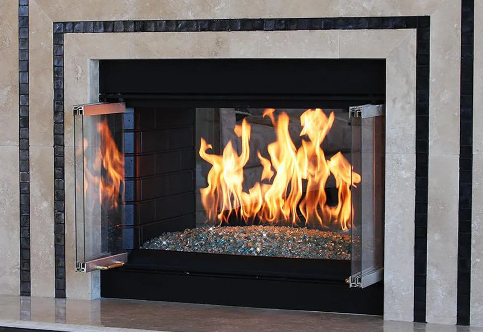 Contemporary gas fireplace featuring clear glass doors and vibrant flames over blue fire glass media. The sleek black and stone tile surround adds a luxurious touch to indoor living spaces, offering both warmth and modern elegance to home interiors.