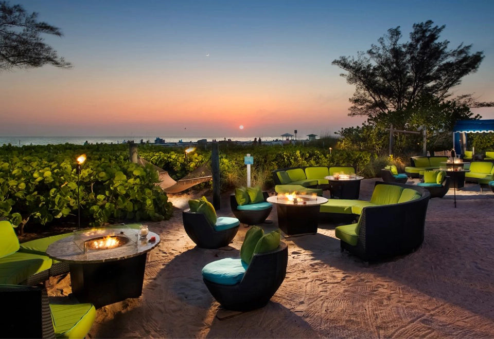 Stunning beachside patio with modern outdoor commercial fire pit tables surrounded by vibrant green and black seating. The cozy fire pits create a warm and inviting ambiance, ideal for outdoor dining, evening gatherings, and enhancing commercial outdoor spaces with style and comfort.