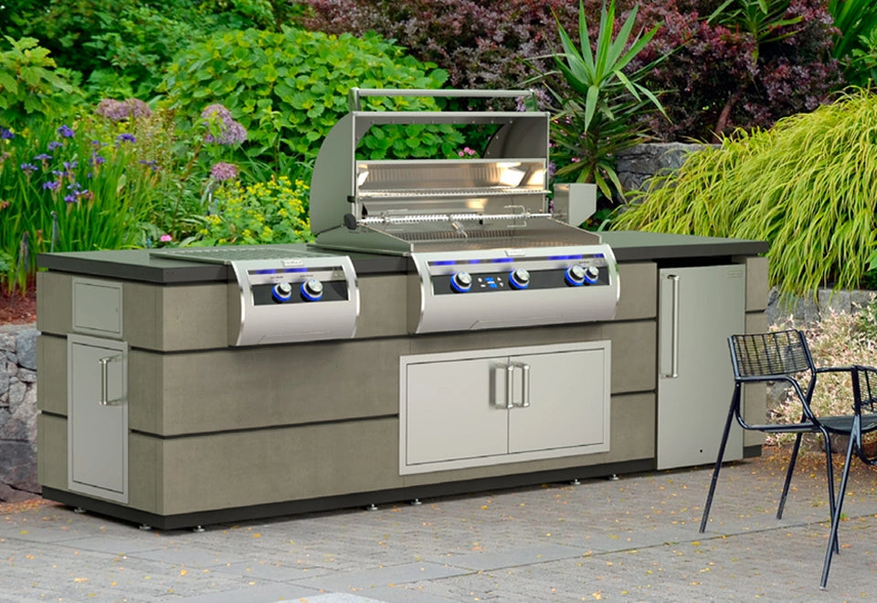 Modern outdoor kitchen grill station featuring stainless steel appliances, built-in insulation jackets, and a sleek concrete finish surrounded by lush greenery.