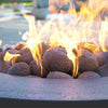 Close-up of Starfire Designs rolled lava rocks with flames rising from a fire pit. The outdoor lava rocks, sized between 1-5 inches, create a beautiful fire display with their natural rugged texture and excellent heat retention. These high-quality lava rocks are perfect for outdoor fire pits, adding both functionality and a striking aesthetic