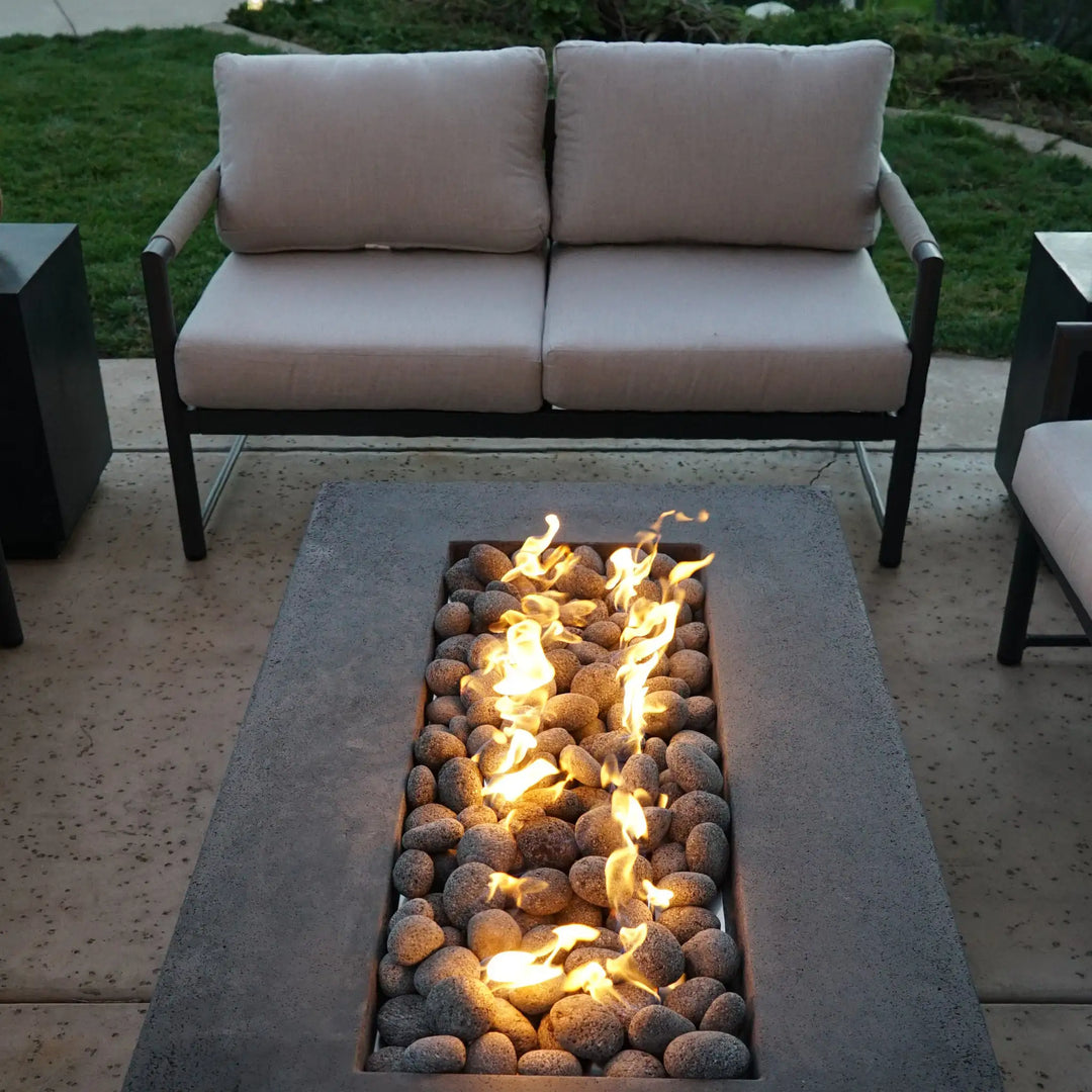 Starfire Designs rolled lava rocks used in a rectangular fire pit on a patio, surrounded by modern outdoor furniture. The medium-sized lava rocks (2-3 inches) offer both heat efficiency and a rugged, natural appearance, making them an excellent choice for stylish outdoor fire features.