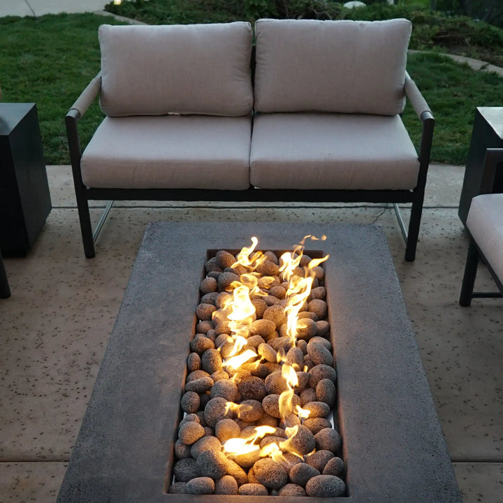 Starfire Designs rolled lava rocks used in a rectangular fire pit on a patio, surrounded by modern outdoor furniture. The medium-sized lava rocks (2-3 inches) offer both heat efficiency and a rugged, natural appearance, making them an excellent choice for stylish outdoor fire features.