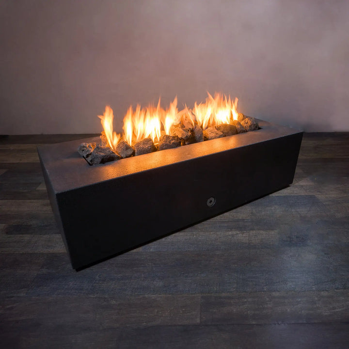 A stunning lifestyle image of large outdoor volcanic lava rocks arranged in a sleek rectangular fire pit. The black fire pit features flickering flames rising beautifully between the rugged dark-colored lava rocks, adding warmth and ambiance. Ideal for outdoor fire pit setups, the 10 lbs of large lava rocks provide an earthy and natural aesthetic. Perfect for enhancing the look of any fire feature, these volcanic rocks are designed for durability in heat and flames, making them a great choice for outdoor fi