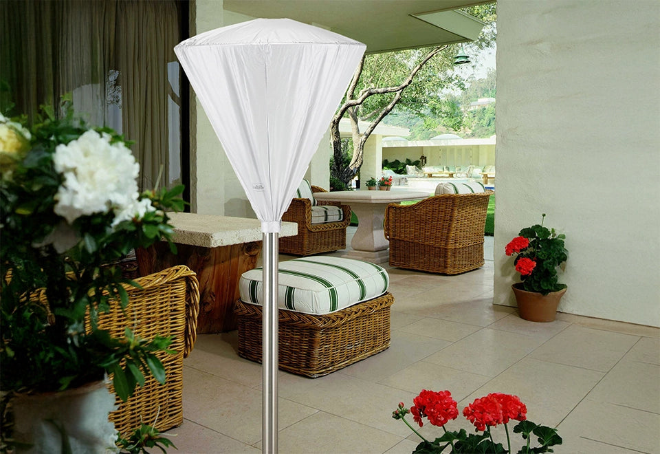 White weather-resistant patio heater cover protecting a tall outdoor heater in a beautifully decorated patio with wicker furniture and vibrant flowers