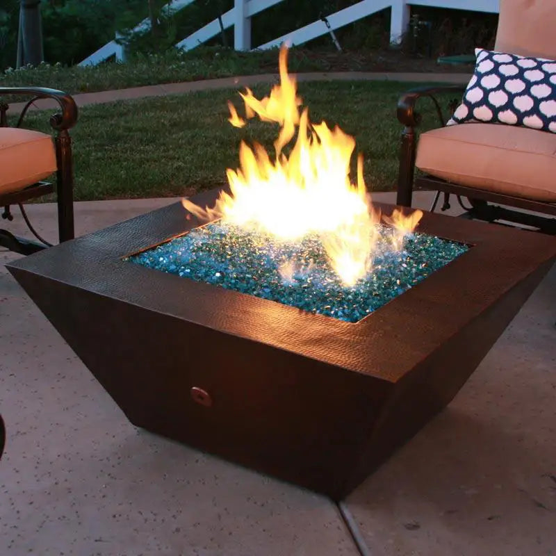 Plaza Moreno 40" x 40" square copper fire pit glowing with blue fire glass and flames in an outdoor patio setting, perfect for evening backyard gatherings by Starfire Designs