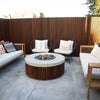 The Prism Hardscapes Hampton Fire Bowl enhances a cozy outdoor seating area, surrounded by comfortable chairs and stylish wooden fencing. The round fire bowl, with its concrete top and wooden slat panels, provides a perfect ambiance for intimate gatherings. Designed for patio fire pits, outdoor lounging, and creating a stylish yet functional fire pit area. Ideal for those seeking a modern fire pit for their outdoor space, featuring gas fire bowls and warm backyard aesthetics.