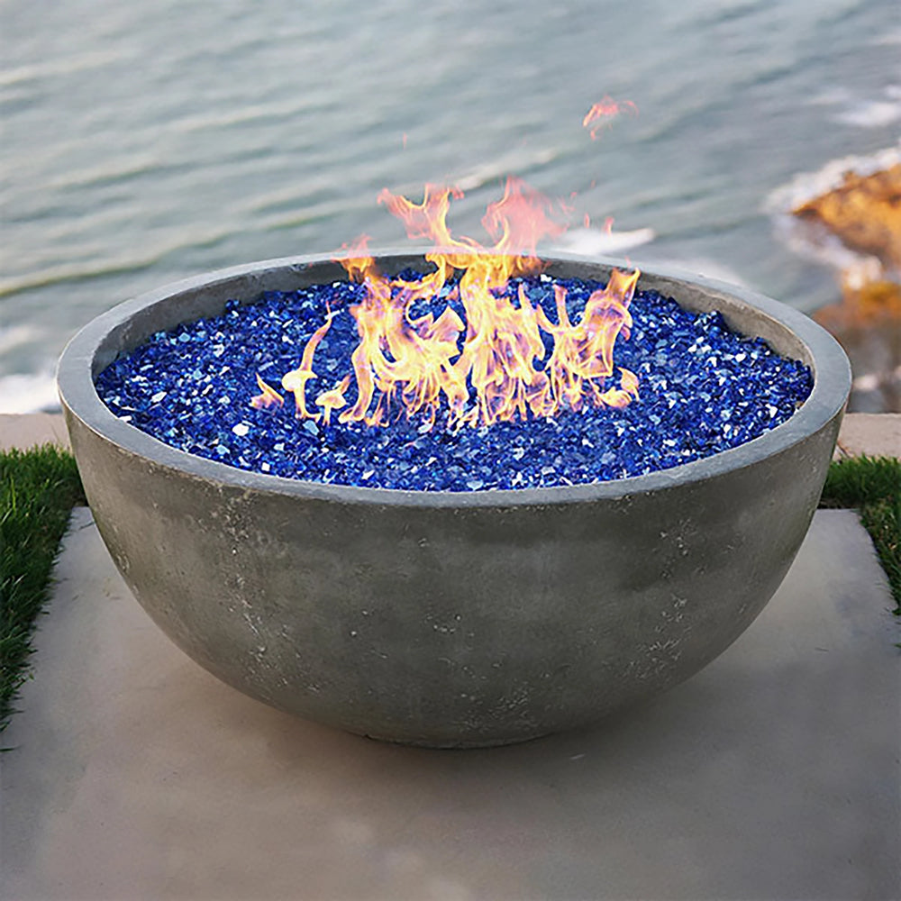 Prism Hardscapes Moderno 1 Gas Fire Bowl placed in a coastal setting, filled with vibrant blue fire glass, offering a modern and stunning visual experience. This natural gas fire pit is ideal for creating a luxurious outdoor ambiance, blending perfectly with waterfront properties or high-end backyard spaces. A must-have for large outdoor patios or resorts
