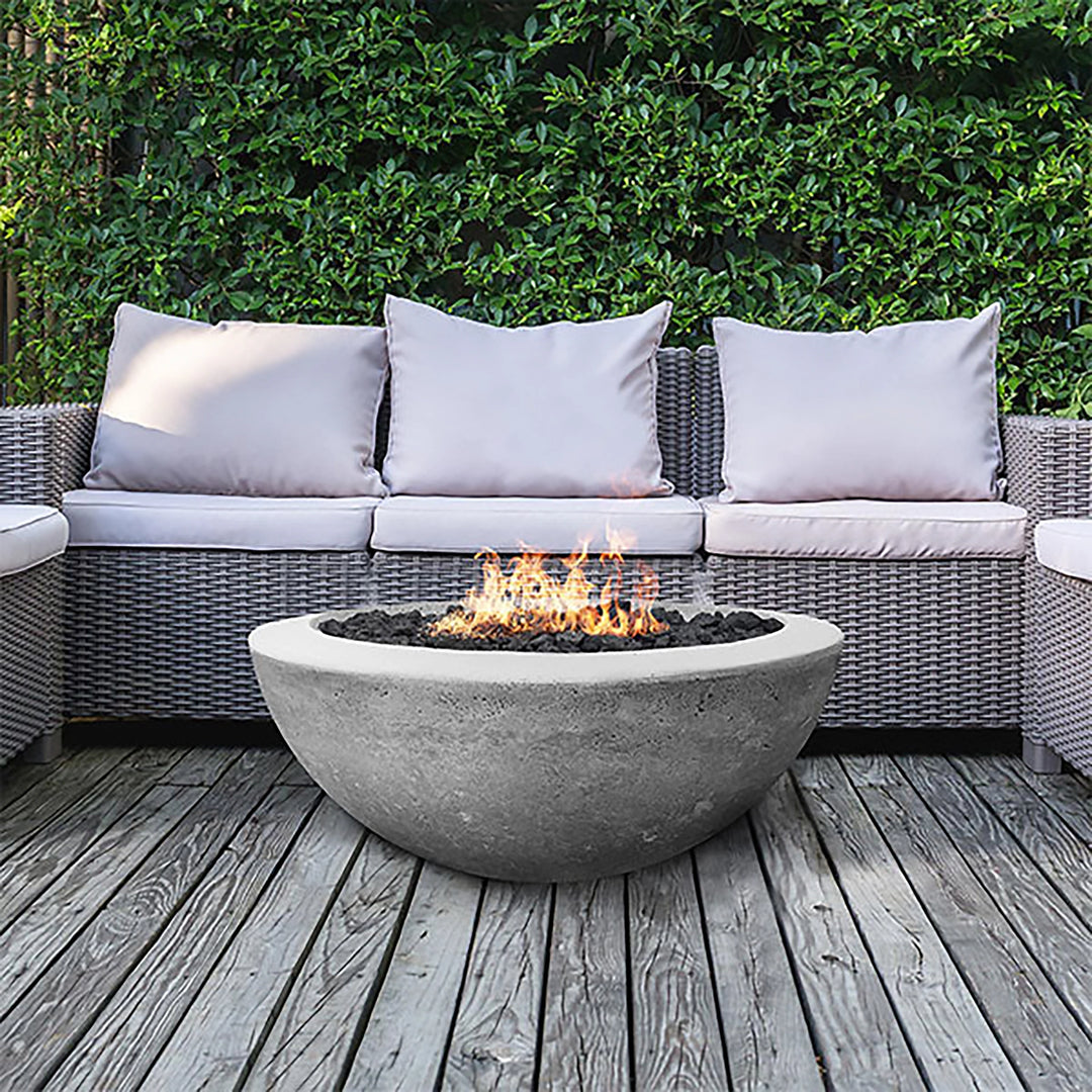 rism Hardscapes Moderno 2 Gas Fire Bowl in pewter gray on a wooden deck with sleek modern gray furniture. The round concrete fire bowl creates a welcoming focal point for outdoor entertaining, making it perfect for outdoor gas fire pits, modern fire pits, and patio fire pit tables, bringing warmth and ambiance to any outdoor living space.